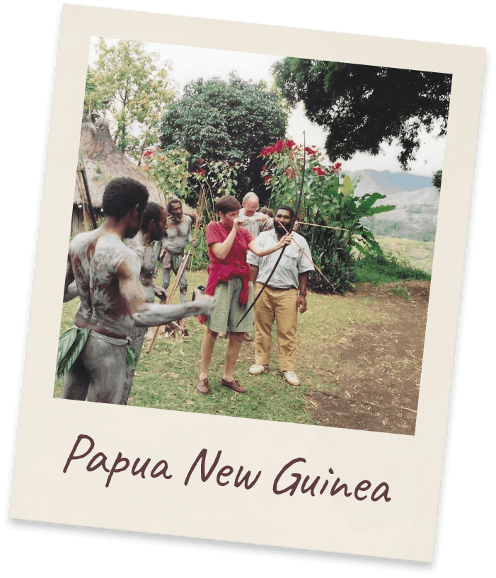 Papua New Guinea. Highland villagers in traditional dress with spears beside two Western men, one holding a baby, green hills behind.