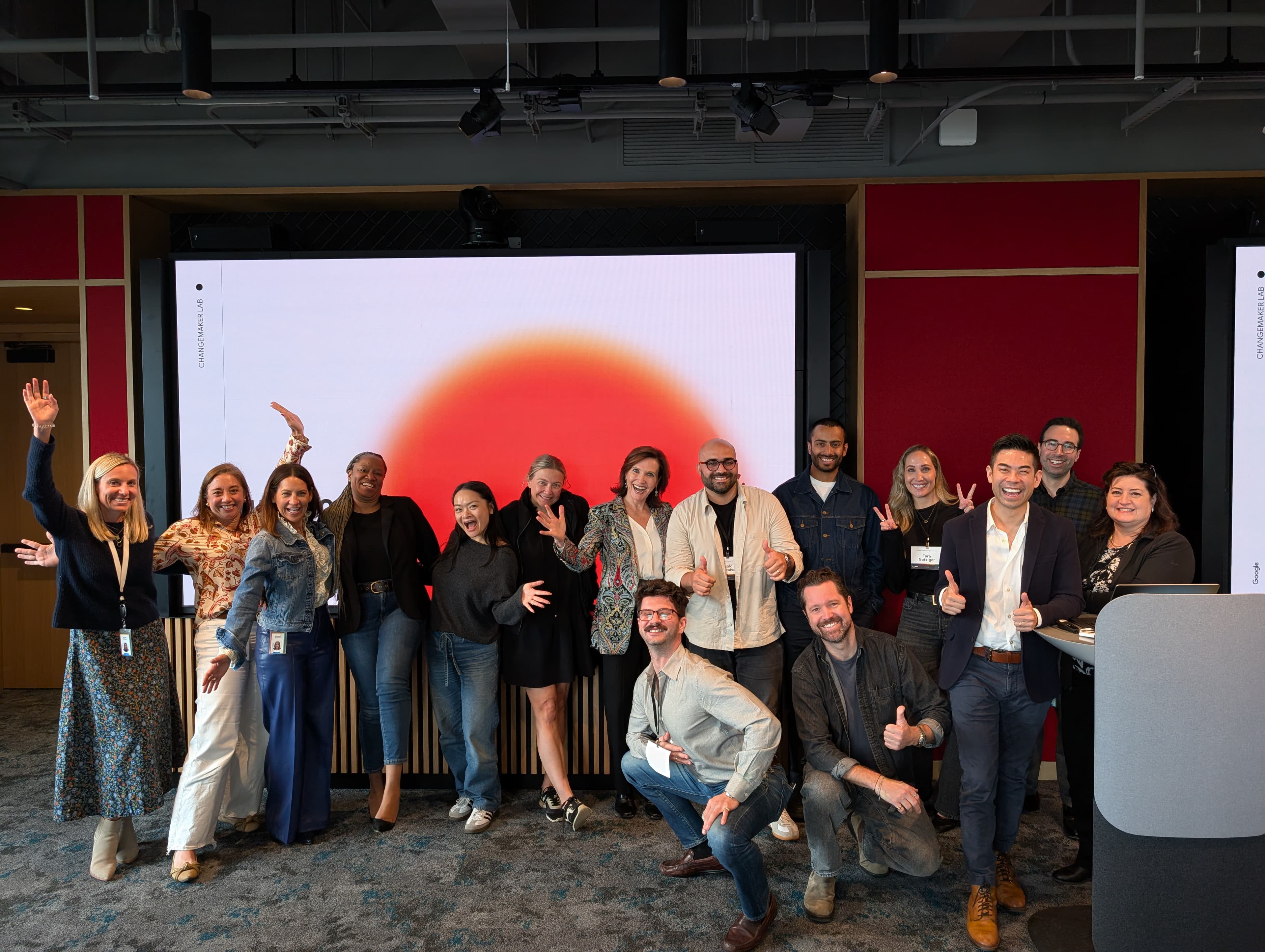 Margie Warrell celebrating on stage with a team of about seven people, a large red sun graphic projected behind them