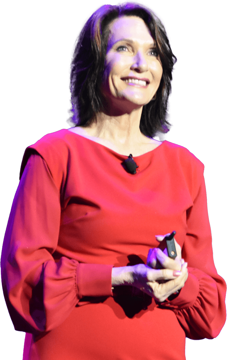 Dr. Margie Warrell on stage in a red dress, smiling and looking up, hands clasped around a presentation clicker