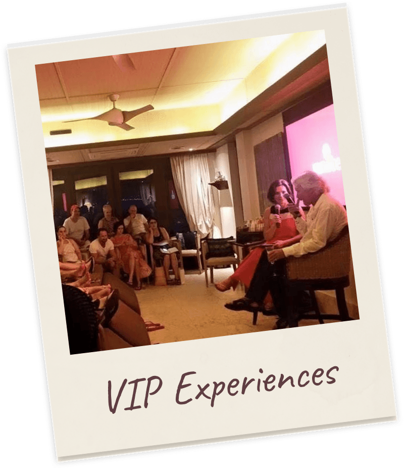 Polaroid captioned “VIP Experiences”: a warm-lit hotel function room packed with a seated audience, with Dr. Margie Warrell in conversation in an armchair at the far end beside a magenta-lit screen